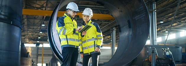 Male and Female Industrial Engineers in Hard Hats Discuss New Project while Using Tablet Computer